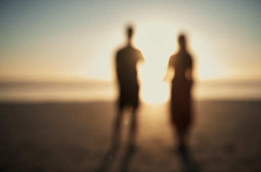 Two blurry people couple standing watching the sunset sunrise on holiday at the beach