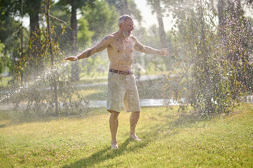 Refreshing shower. A half-naked man in shorts standing under shower in the park