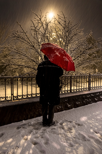 The man with the red umbrella is waiting under the snowfall. Selctive Focus Man. hopeless wait