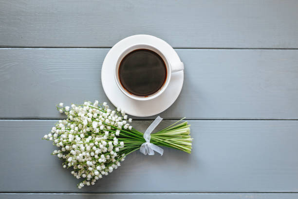 Bouquet of Lily of the valley flowers and cup of coffee on grey wooden background. stock photo