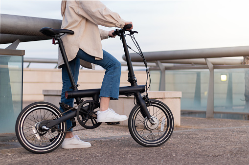 Zero emission concept. Cropped woman legs riding an electric bicycle as transport around the city wearing a casual outfit