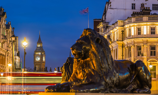 The iconic clocks of Big Ben overlooking Whitehall and the Landseer’s Lions of Nelson’s Column in Trafalgar Square in the heart of London illuminated at night.