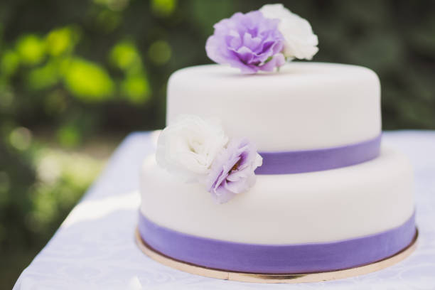 istock White wedding cake with purple decoration outdoors on the table. 1394415091