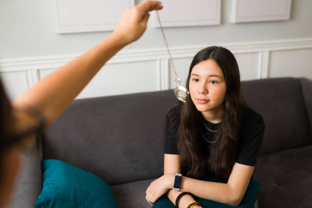 Therapist hypnotizing a patient to help with depression Caucasian teenage girl looking at a clock to get hypnotized during a therapy session. Therapist hand using a clock to hypnotize a teen patient hypnosis stock pictures, royalty-free photos & images