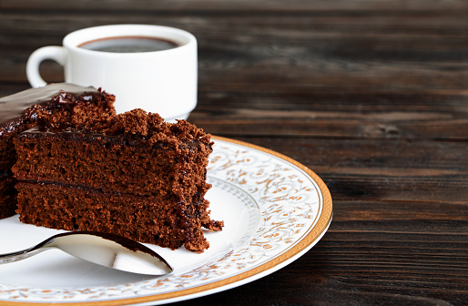 A piece of Chocolate cake on a plate and cup of black coffee on a wooden background.Slice of Homemade brownie cake.Copy space.