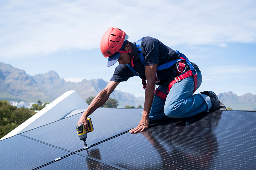 A skilled worker fastens solar panels to the roof of a residential house in Cape Town, South Africa