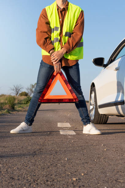 istock Front vertical view of young unrecognizable men holding a red warning triangle with broken car on the side 1394425940
