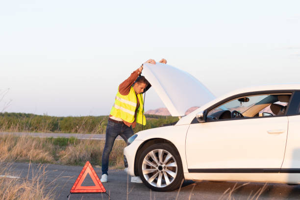 junger mann auf einer weste, der sich nach einer panne am straßenrand auf dem land auf eine offene motorhaube stützt - vehicle breakdown car stranded broken stock-fotos und bilder