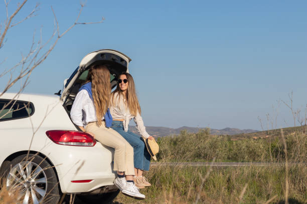 istock Friends sitting in a white car boot, taking a break from driving while on a spring road trip. In a gren landscape 1394426097