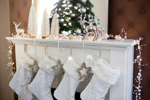 White Christmas socks and silver stars with bells hanging on fireplace. Christmas gifts in socks