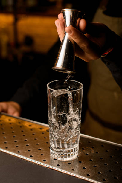 istock Clear glass with ice cube on bar and male hand pouring beverage from jigger 1394431620
