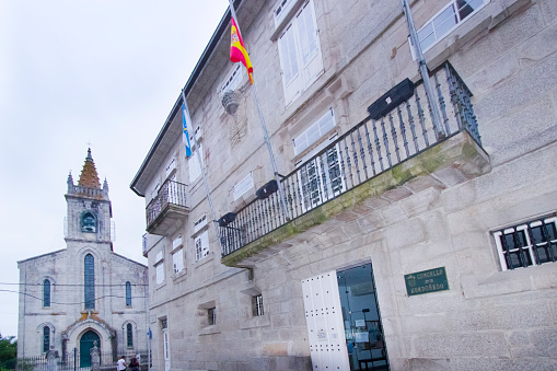 Mondoñedo, Lugo, Spain- August 10, 2022: Town hall in Mondoñedo, facade with balcony and flags, Lugo province , Galicia, Spain. Santiago church in the background.