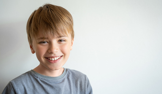 Portrait of smiling child, teenager in grey t-shirt looking at camera over white background. Positive mood.