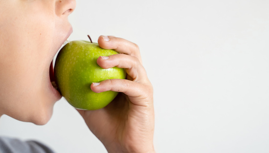 Close up mouth of child biting green apple, isolated over white background. Copy space.
