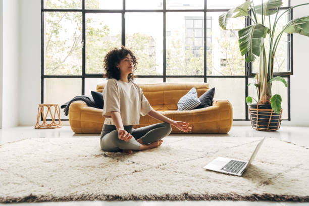 młoda wielorasowa latynoska kobieta medytująca w domu z lekcją medytacji wideo online za pomocą laptopa. - wellbeing zdjęcia i obrazy z banku zdjęć