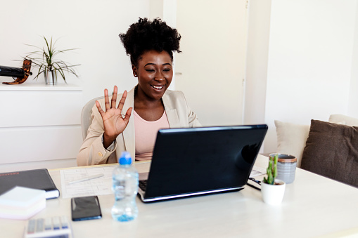 An African woman is using a laptop and working from home. Happy African American businesswoman, looking at laptop screen, holding pleasant conversation with partners clients online, working remotely at workplace.