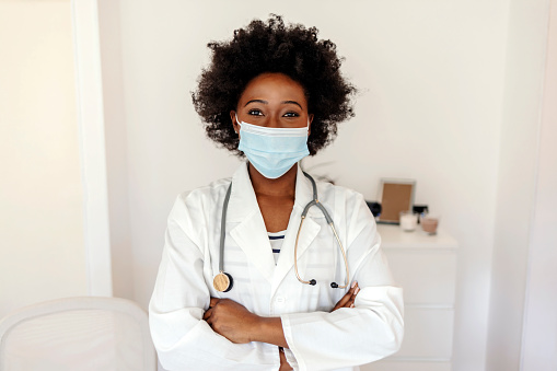 Portrait of a young doctor wearing a face mask while working in a hospital. Portrait of a young doctor working in her office. Smiling young female doctor wearing a mask.