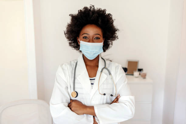 My job is to assist you towards perfect health. Portrait of a young doctor wearing a face mask while working in a hospital. Portrait of a young doctor working in her office. Smiling young female doctor wearing a mask. black hair braiding stock pictures, royalty-free photos & images