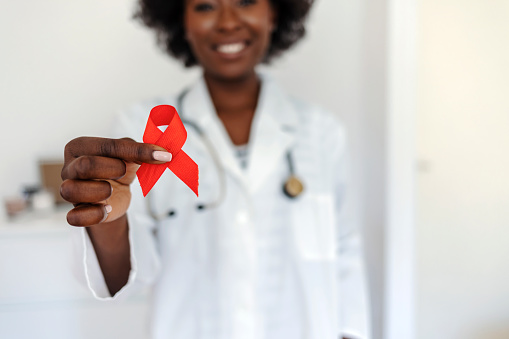 Female doctor with red ribbon. Cancer concept. Doctor Holds Red Ribbon to awareness world aids day Dec. 1. AID, HIV red ribbon. Symbol of awareness, charity, support in disease, illness. Woman doctor holding a red ribbon in her hands.