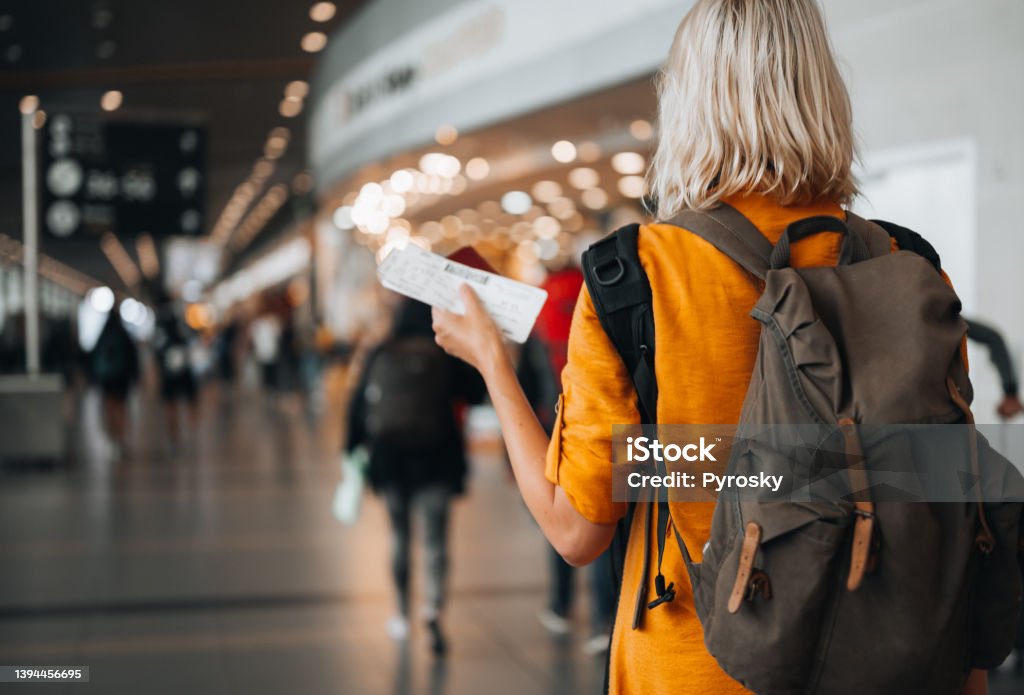 A woman at the airport holding a passport with a boarding pass Rear view of a  woman at the airport holding a passport with a boarding pass as she walks to her departure gate Airport Stock Photo