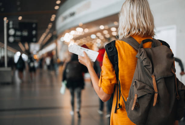 A woman at the airport holding a passport with a boarding pass Rear view of a  woman at the airport holding a passport with a boarding pass as she walks to her departure gate  Traveling stock pictures, royalty-free photos & images