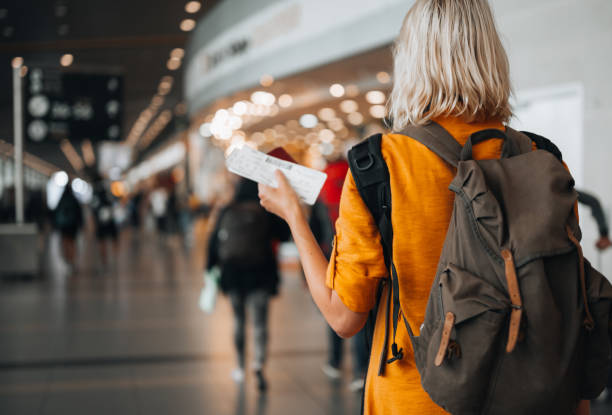 A woman at the airport holding a passport with a boarding pass Rear view of a  woman at the airport holding a passport with a boarding pass as she walks to her departure gate luggage stock pictures, royalty-free photos & images