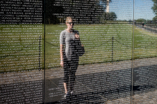 Washington DC, USA - October 6, 2015: A woman observing her reflection in the black marble engraved list of fall soldier names on the Vietnam memorial wall national moment in Washington, DC managed by the National Park Service.