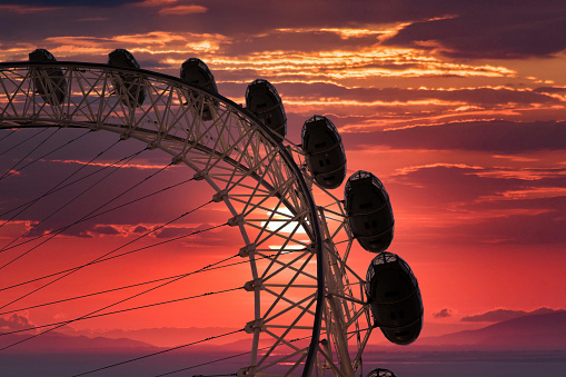 London, United Kingdom - June 3, 2018: The London Eye Millennium Wheel, designed by Marks Barfield, silhouetted pod capsules against a deep red sunset in the central district of London in the United Kingdom.