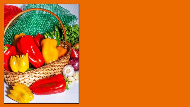 Composition with assorted raw organic vegetables. Red peppers, green peppers, yellow peppers, red onions, garlic and parsley inside a wicker basket. Detox diet. Orange Space for advertisement.