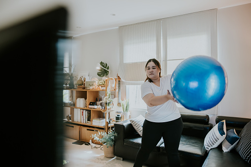 Passion to be fit, Thai obese woman working out with exercise ball at her home on weekend.