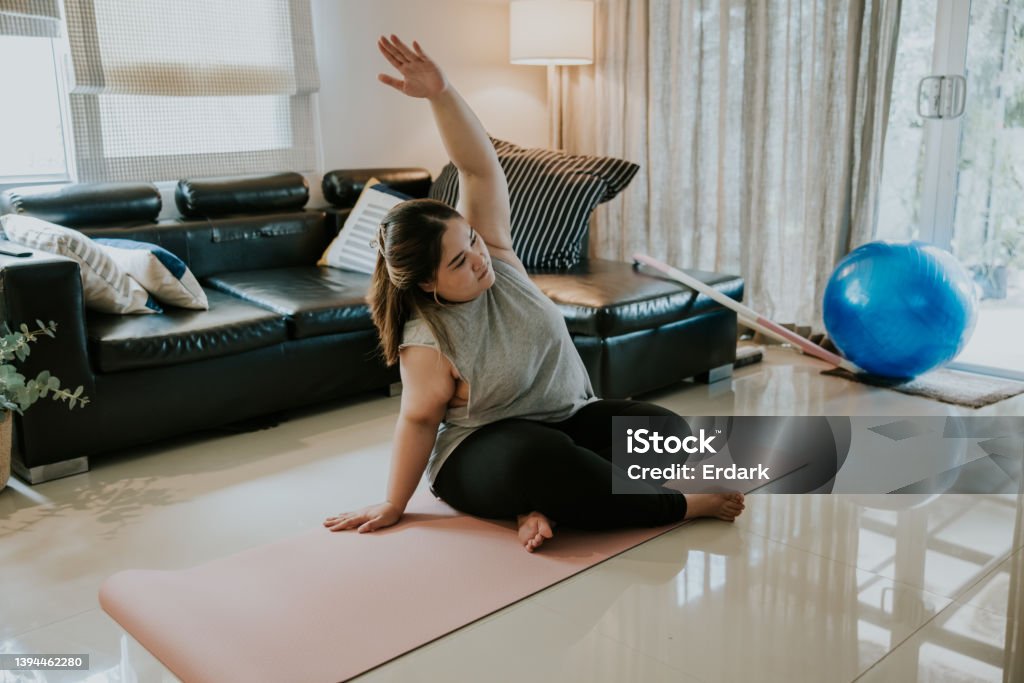 Online yoga class for beginner at home. Hand stretching with plus size girl, Thai young adult woman watching on television and doing following by step with her online yoga class. Yoga Stock Photo