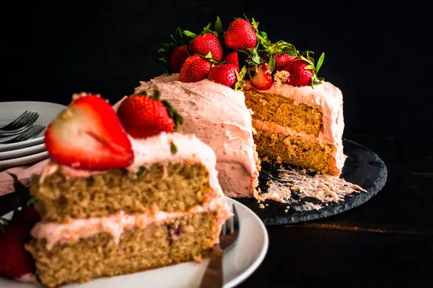 Focus on a strawberry cake with a fresh slice in the foreground