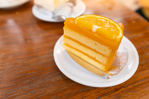Sweet or dessert, a delicious orange cake topping with orange slices on white plate on wooden table with a cafe environment.