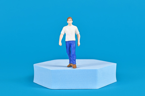 Man figure with shirt and jeans on pedestal in front of blue background