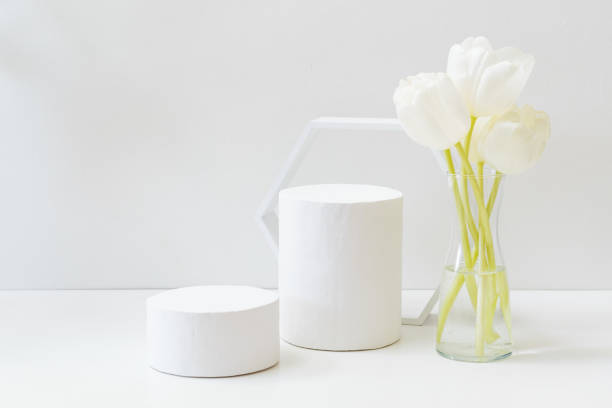 istock Geometric podium or pedestal with white spring tulips in a vase on a white background. Empty podium for product presentation 1394477457
