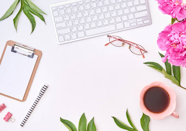 istock Feminine blogger workplace with notepad, clipboard, cup of coffee and pink peonies on a white table. Flat lay banner,  template for blog 1394477458