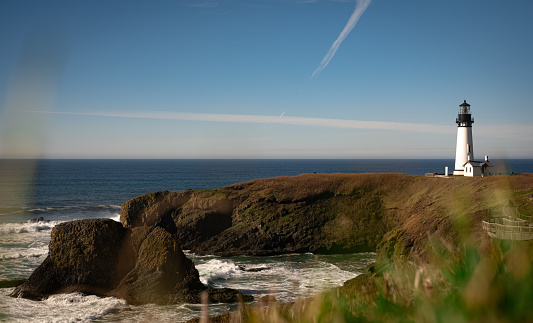A stunning view of the iconic Yaquina Head Lighthouse off of Oregons breathtaking coast. The waves of the pacific ocean crashing into the sea stacks below the cliffs.