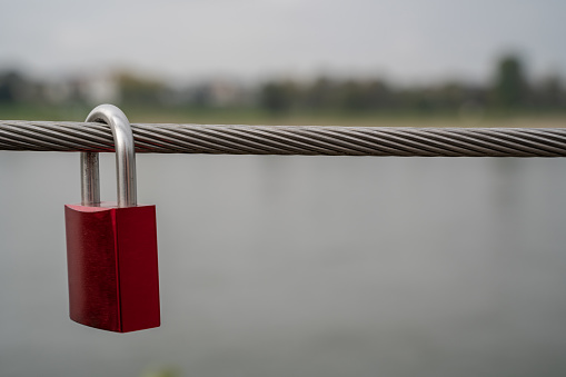 Steel cable from a railing on the bridge with an attached red padlock