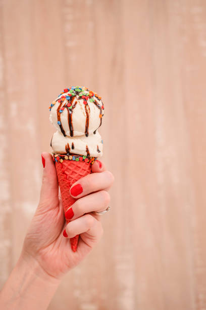 istock Woman's hand holding vanilla ice cream in red waffle cone 1394480660