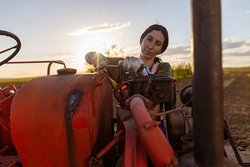 Hispanic girl waving hand while pretending to drive a red tractor agricultural field