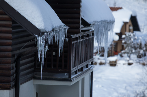 Copy space shot of tick icicles hanging from the snow covered rooftop on a rustic log cabin on a cold winter day.