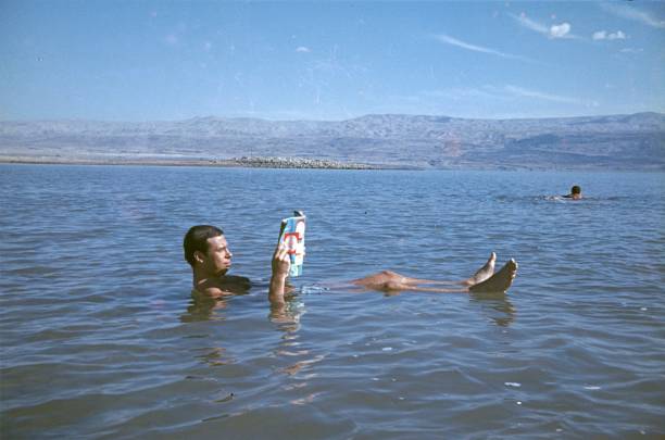 un uomo legge una rivista mentre nuota nel mar morto - historical person foto e immagini stock