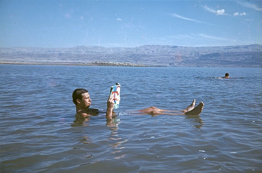 Dead Sea, Israel, 1975. A man reads a magazine while swimming in the Dead Sea.