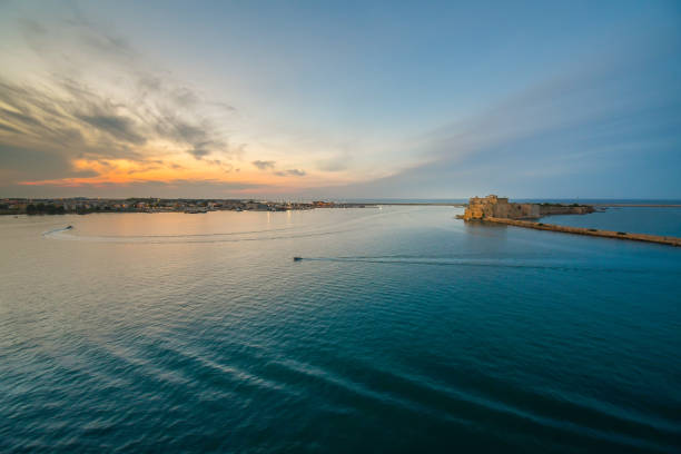 sonnenuntergang in der adria direkt vor dem kreuzfahrthafen und hafen von brindisi italien in der region apulien mit der burg alfonsino im blick von einem kreuzfahrtschiff auf see. - brindisi stock-fotos und bilder