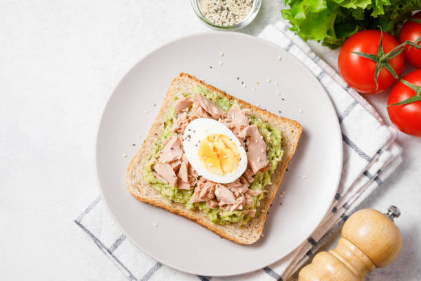 istock Avocado rye bread toast with tuna and boiled egg on bright background. Healthy appetizer, breakfast, lunch or snack. Top view 1394500391
