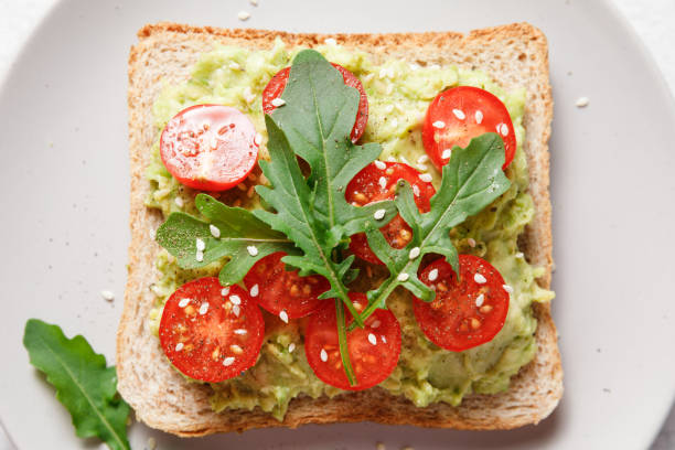istock Avocado rye bread toast with cherry tomatoes and arugula on bright background. Healthy appetizer, breakfast, lunch or snack. Vegan food concept. Close up, top view 1394500392