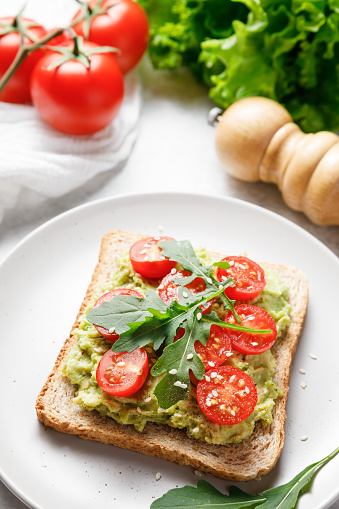 Avocado rye bread toast with cherry tomatoes and arugula on bright background. Healthy appetizer, breakfast, lunch or snack. Vegan food concept. Close up.