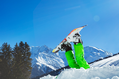 Snowboarder with head stuck in the snow, legs and snowboard in the air over Alpine tops on background