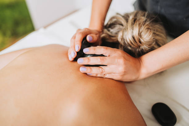 Therapist placing hot spa volcanic lava stone on a female patient's neck. Energy stones. Hot spa volcanic lava stone placed on a female patient's neck and back, by a physiotherapist. Medical massage. High quality photo. Horizontal. Health care. hot stone massage stock pictures, royalty-free photos & images