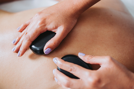 Hot spa volcanic lava stone placed on a female patient's neck and back, by a physiotherapist. Medical massage. High quality photo. Horizontal. Health care.